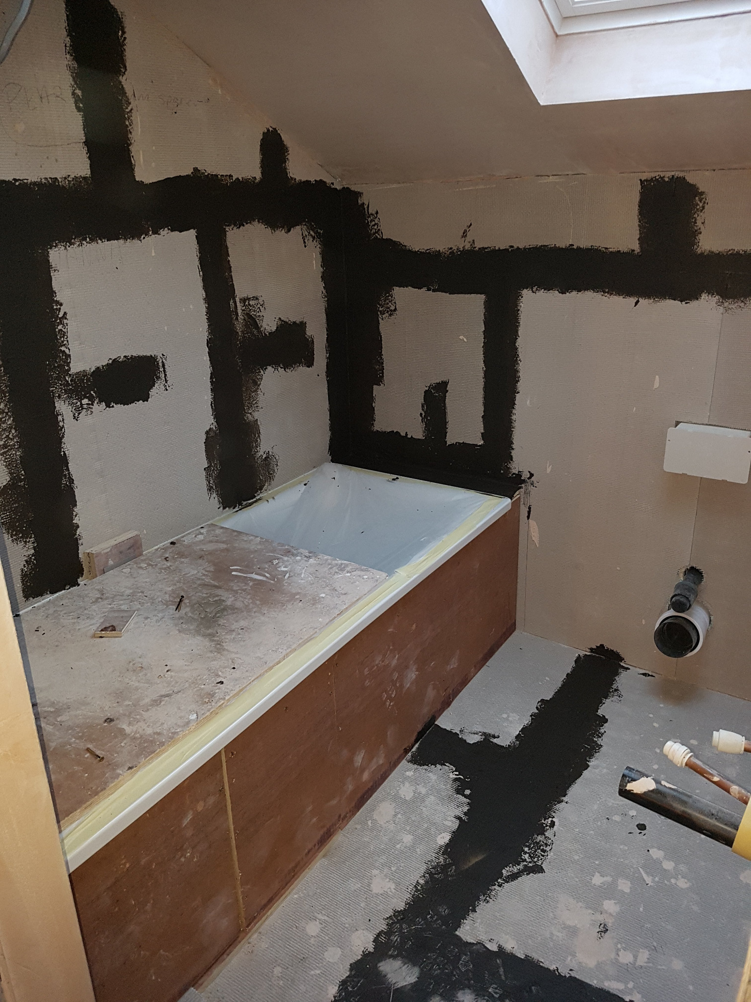 Przygotowanie do hydroizolacji ścian i podłogi w łazience w Lublinie, widoczna wanna obudowana płytami oraz nałożona czarna powłoka izolacyjna.