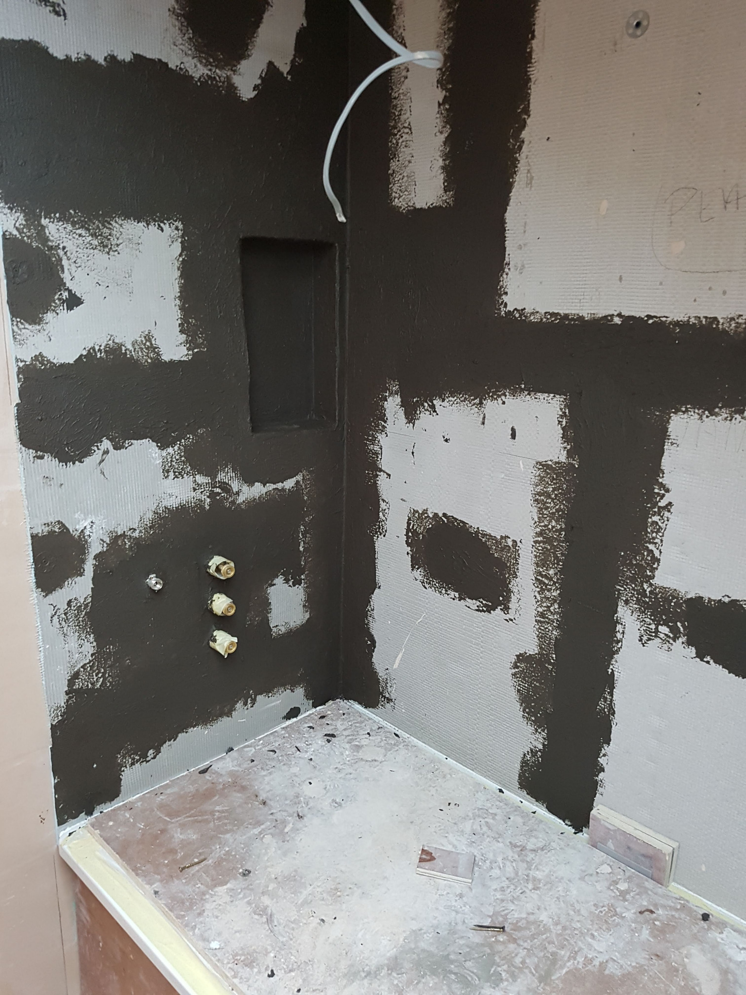 Przygotowanie ścian łazienki pod płytki: hydroizolacja w narożniku z wnęką, widoczne wystające rury instalacji wodnej.