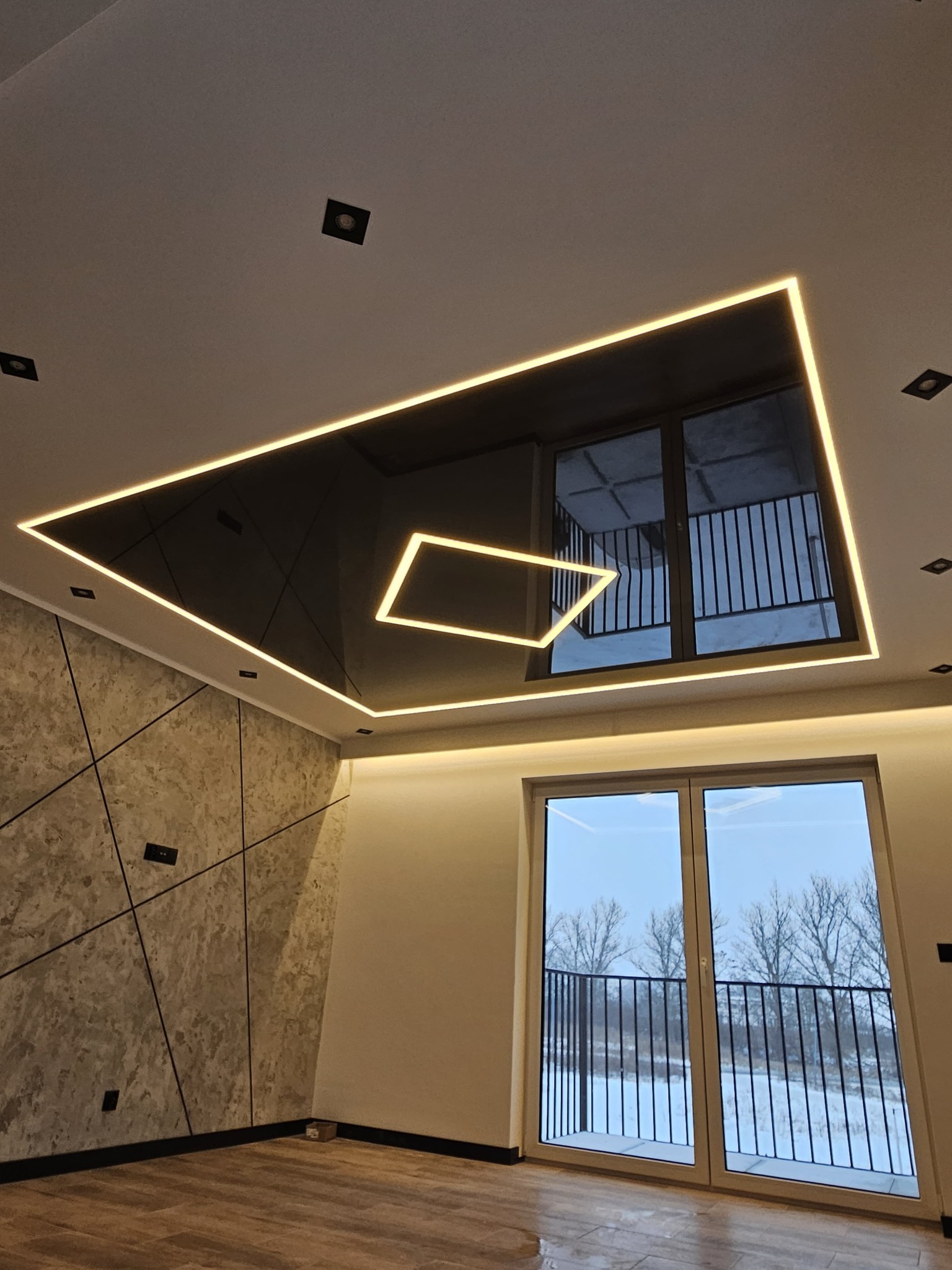 Nowoczesny sufit napinany z podświetleniem LED w kształcie prostokąta, widok z dołu, Złotów. Czarny połysk sufitu odbija okno balkonowe.