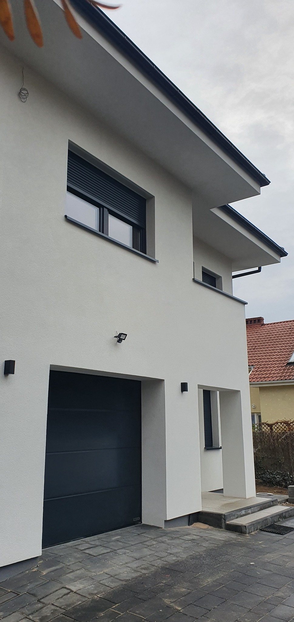 Nowoczesny dom z białą elewacją, antracytowymi elementami wykończeniowymi i bramą garażową, widok z dołu na fragment budynku.