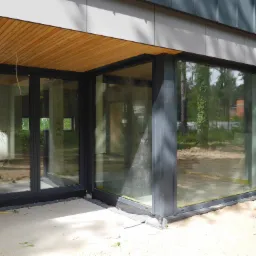 Nowoczesna bryła budynku z dużymi, przesuwnymi oknami aluminiowymi w kolorze antracytowym, widok z zewnątrz, widoczne drewniane wykończenia podbitki i elewacji.