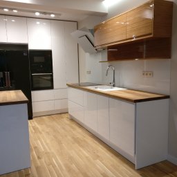 Lewkowicz Meble Kuchnie&Szafy - Nowoczesna kuchnia z białymi, lakierowanymi frontami szafek dolnych i drewnianymi blatami, uzupełniona o górne szafki z forniru bambusowego oraz czarny sprzęt AGD w zabudowie.