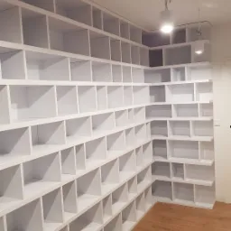 Biała, modułowa szafa wnękowa z licznymi półkami, oświetlona punktowo, z drewnianą podłogą.