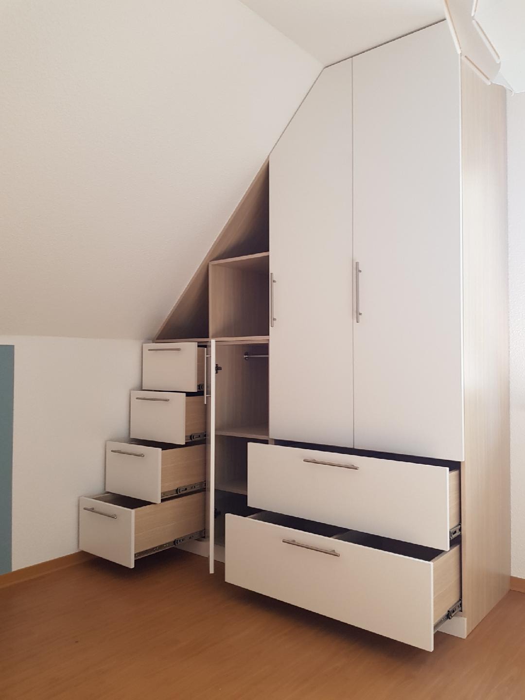 Biała szafa wnękowa pod skosem dachu z otwartymi szufladami i półkami, widoczne prowadnice szuflad, minimalistyczne uchwyty.