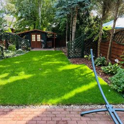 DM CONCEPT DANIEL MARKOWSKI - Wypielęgnowany trawnik z drewnianą altaną w tle, obrzeże z kostki brukowej i fragment stelaża do hamaka.