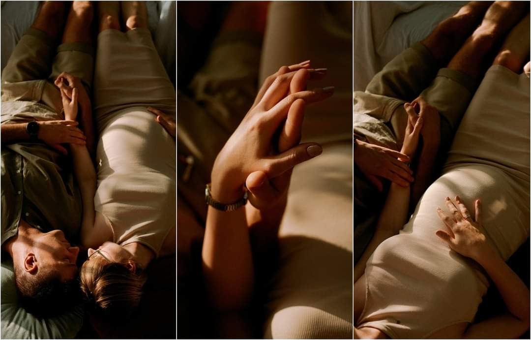 Stylizowana sesja ciążowa w ciepłych barwach: przyszli rodzice leżą blisko, trzymając się za ręce, dłoń kobiety spoczywa na brzuchu, delikatne światło podkreśla zaokrąglony kształt sukienki.