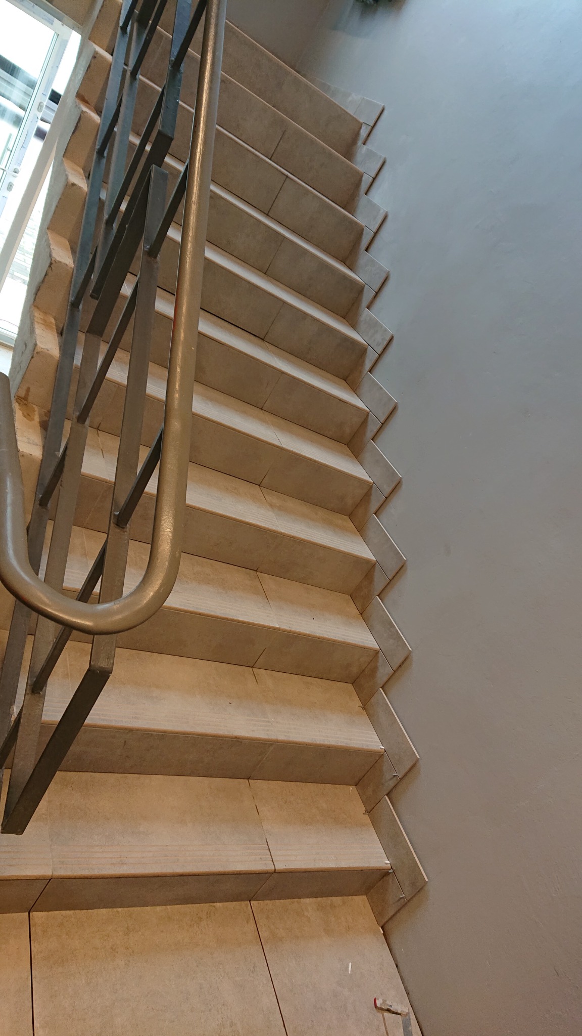 Wykończone schody wyłożone płytkami ceramicznymi we Wrocławiu, z metalową balustradą, widoczne z góry pod kątem, prezentujące staranne ułożenie płytek i estetyczne połączenie ze ścianą.