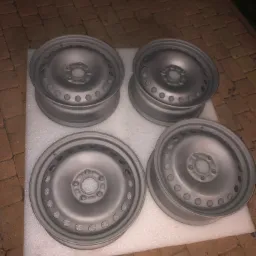 Cztery stalowe felgi samochodowe po obróbce, leżące na białej piance na tle ceglanej kostki brukowej, widoczne ślady po piaskowaniu.