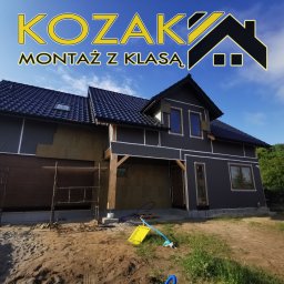 Bartosz Kozak Montaż z klasą - Dom w trakcie ocieplania, widoczne rusztowania, izolacja termiczna na ścianach i logo firmy 'KOZAK MONTAŻ Z KLASĄ' w górnej części kadru.