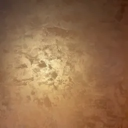 Ściana z efektem dekoracyjnym w odcieniach brązu i złota, z wyraźną fakturą i nierównomiernym oświetleniem.