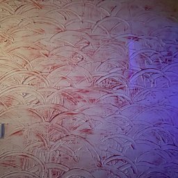 N.P.Air.Sp.Zo.O. - Tekstura ściany w odcieniach czerwieni i fioletu, wykonana techniką dekoracyjną w Poznaniu, przypominająca łuski lub fale.