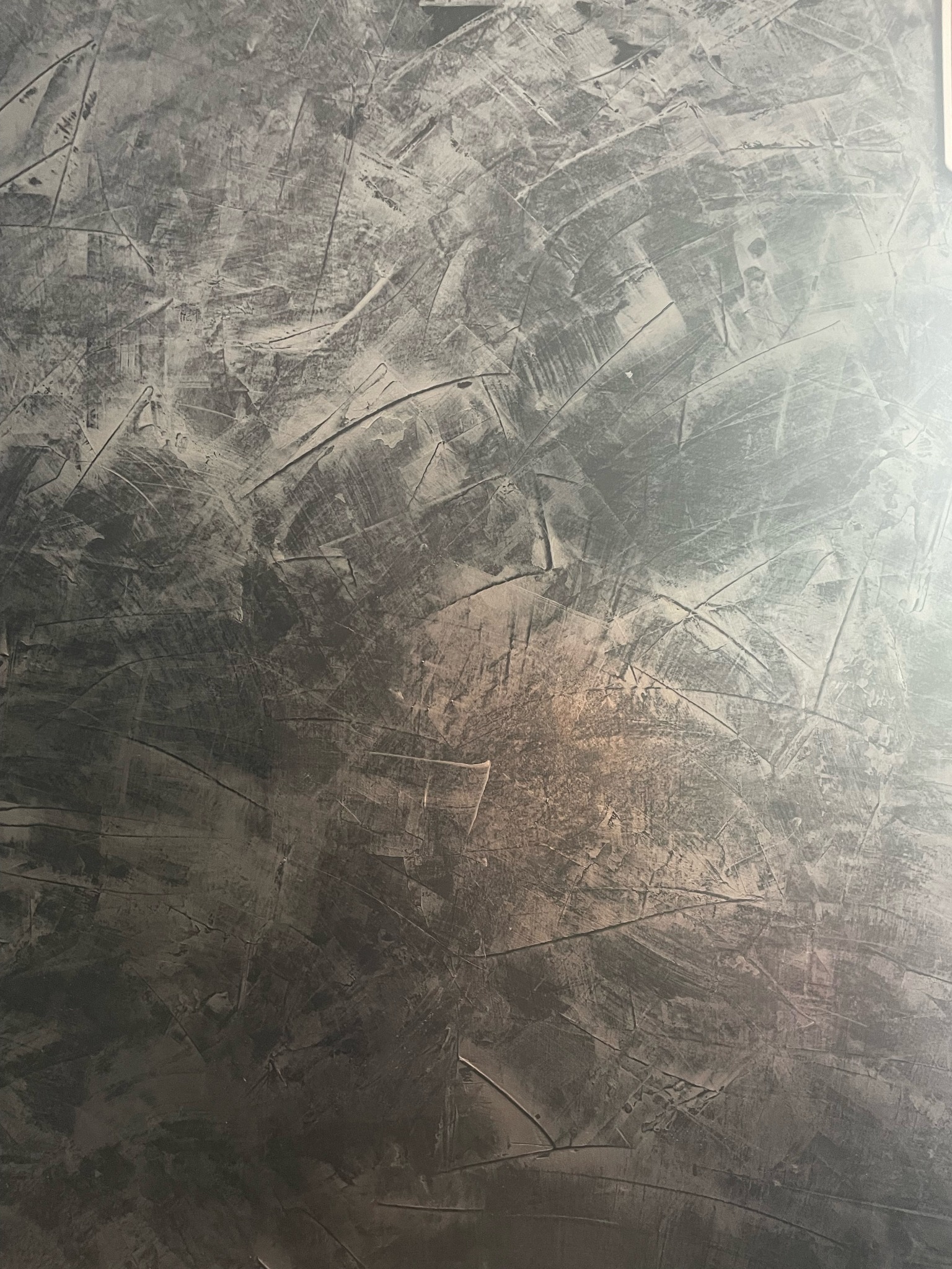 Szara ściana z wyraźną fakturą nałożoną metodą dekoracyjną, widoczne ślady pędzla i szpachelki tworzące nieregularny wzór.