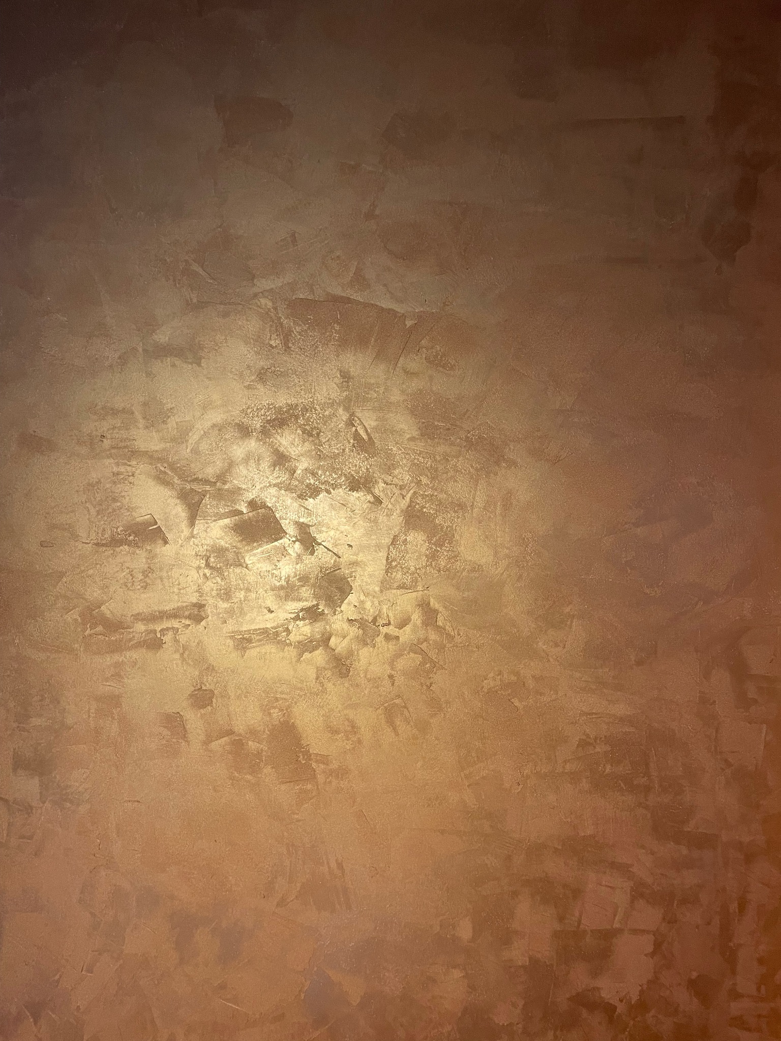 Ściana z efektem dekoracyjnym w odcieniach brązu i złota, z wyraźną fakturą i nierównomiernym oświetleniem.