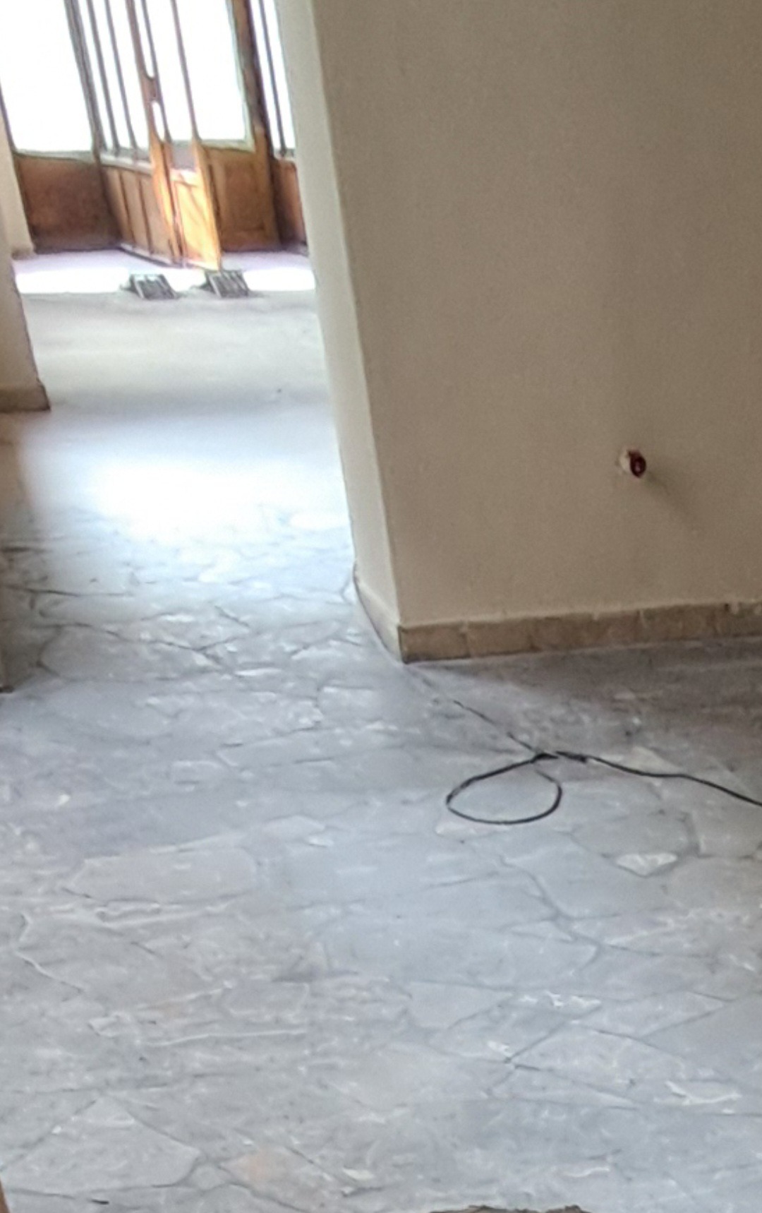 Wyremontowane wnętrze z marmurową posadzką i widocznym gniazdkiem elektrycznym na ścianie. W tle drewniane drzwi balkonowe z szybami.