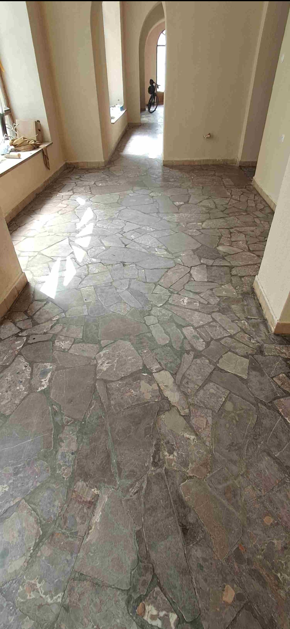 Wykończona podłoga z nieregularnych, szarych kamieni w jasnym wnętrzu z łukowymi przejściami. W tle widoczny rower. Kamienna posadzka po realizacji.