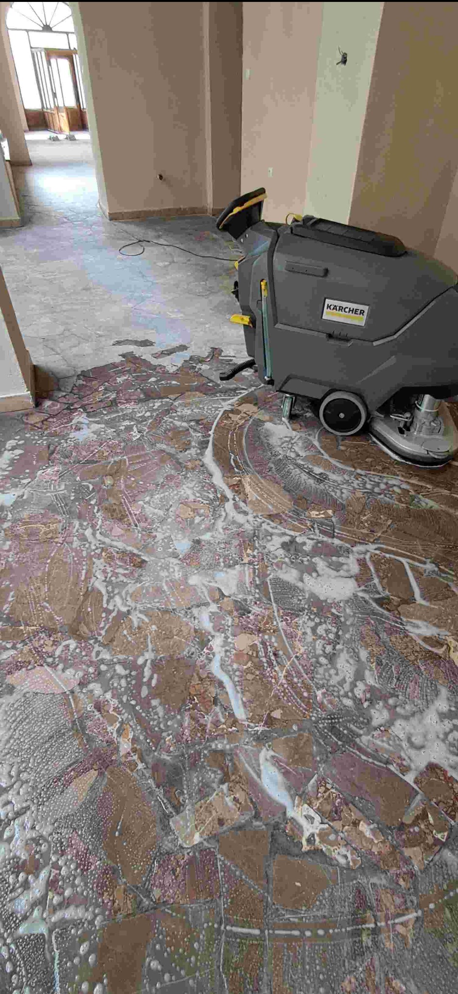 Szorowarka Karcher w trakcie mycia marmurowej posadzki z detergentem, widoczne ślady czyszczenia i piana. Jasne wnętrze budynku w tle.
