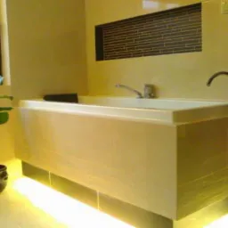 Beżowa wanna z podświetleniem LED i mozaiką na ścianie. Nowoczesna aranżacja łazienki z rośliną doniczkową przy oknie. Bateria umywalkowa zamontowana na wannie.