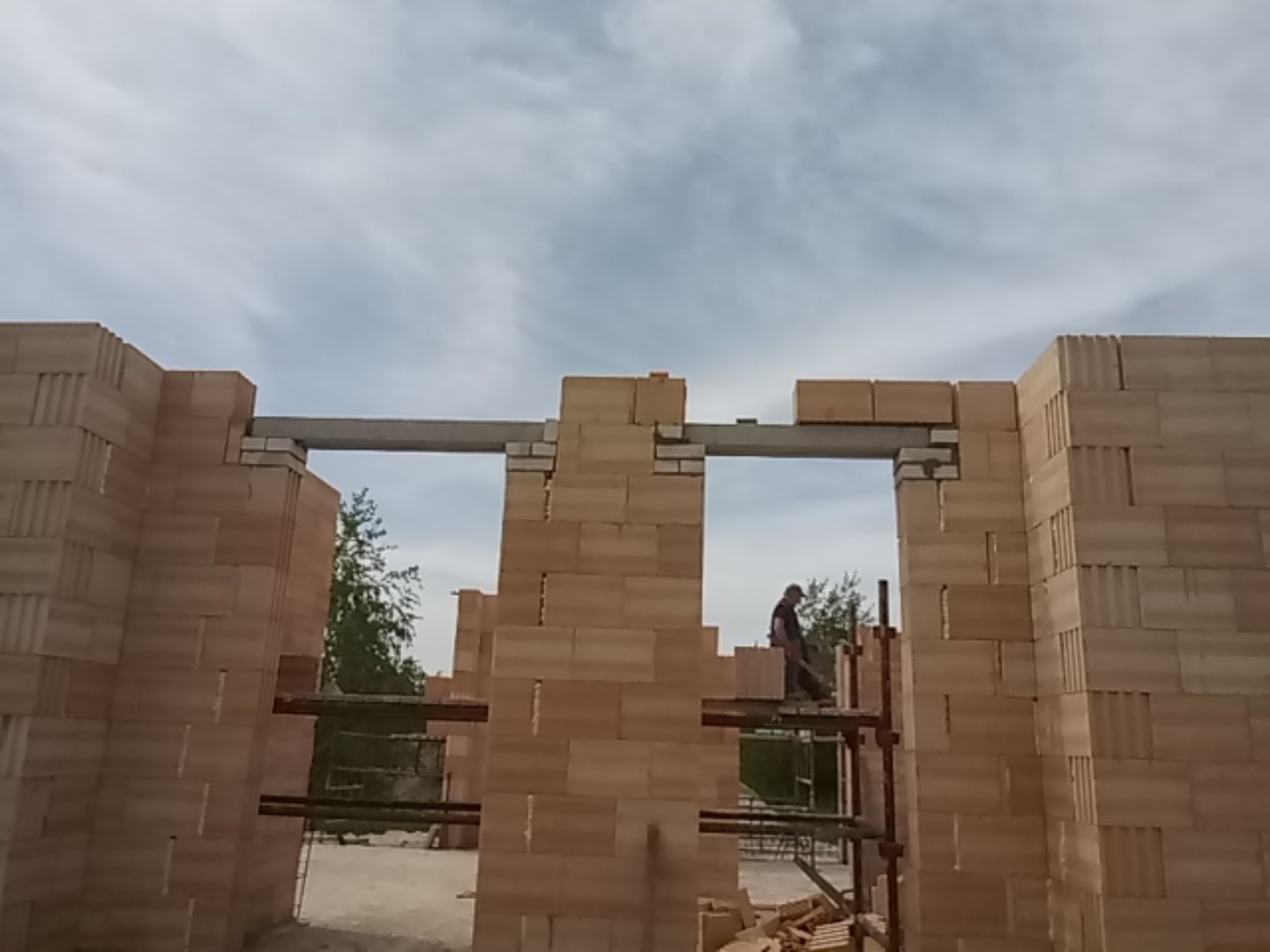 Wznoszenie ścian domu murowanego z bloczków w Nowogrodzie Bobrzańskim, widok na murarza pracującego na rusztowaniu przez otwór okienny z nadprożem.