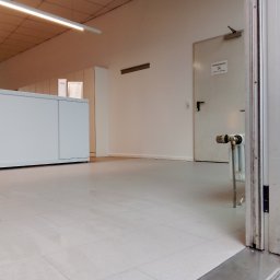 BANAŚ CONSTRUCTION Radosław Banaś - Jasne, płytki podłogowe w nowym biurze, widok z niskiej perspektywy, z fragmentem grzejnika i drzwi w tle, oświetlenie sufitowe LED.