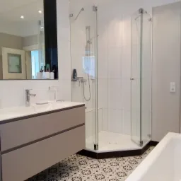 Nowoczesna łazienka z kabiną prysznicową narożną, umywalką z szafką w odcieniach szarości i wzorzystą podłogą w stylu retro.