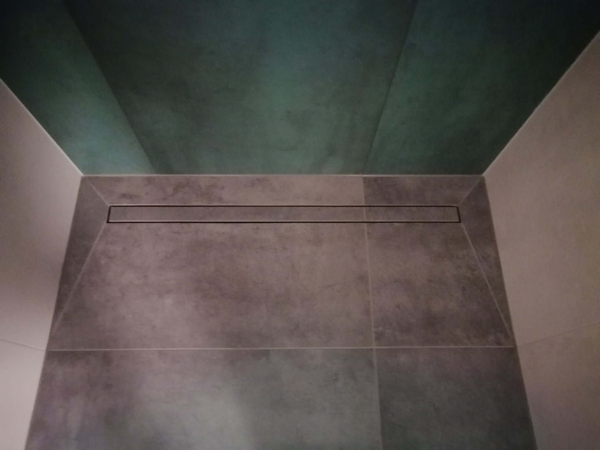 Szare płytki podłogowe i ścienne w kabinie prysznicowej z odpływem liniowym, zielony sufit.