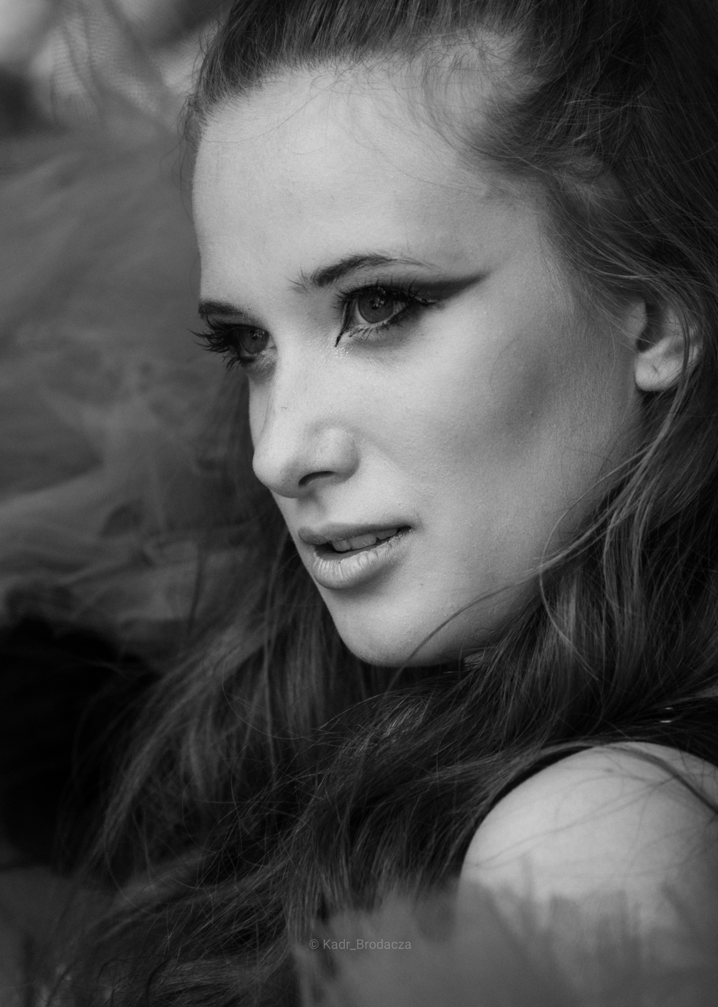 Czarno-biały portret kobiety z mocnym makijażem oczu, spoglądającej w dół, wykonany w Kielcach. Widoczne delikatne rysy twarzy i włosy.