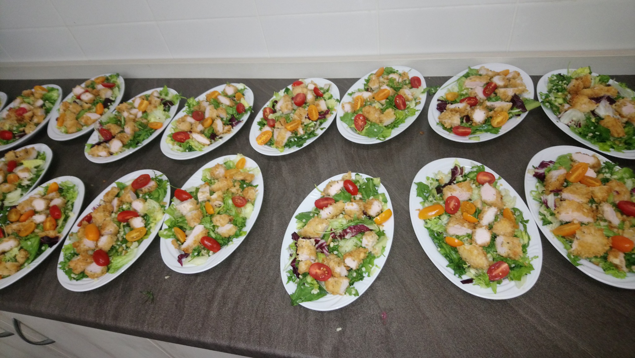 Przygotowane porcje sałatek z kurczakiem, pomidorkami koktajlowymi i zielenią na białych talerzach, gotowe do serwowania w Grudziądzu.