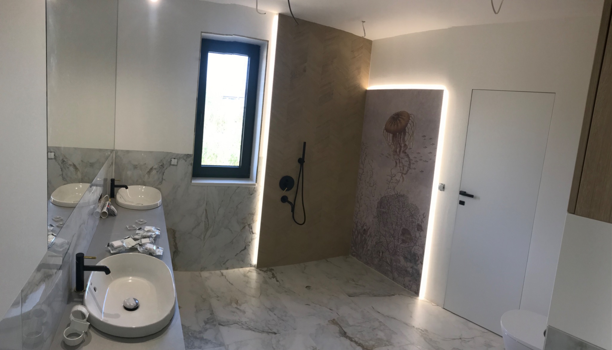 Nowoczesna łazienka z dwoma umywalkami na marmurowym blacie, czarna armatura, podświetlane lustra, prysznic z deszczownicą, dekoracyjna tapeta z motywem meduzy i marmurowa podłoga.