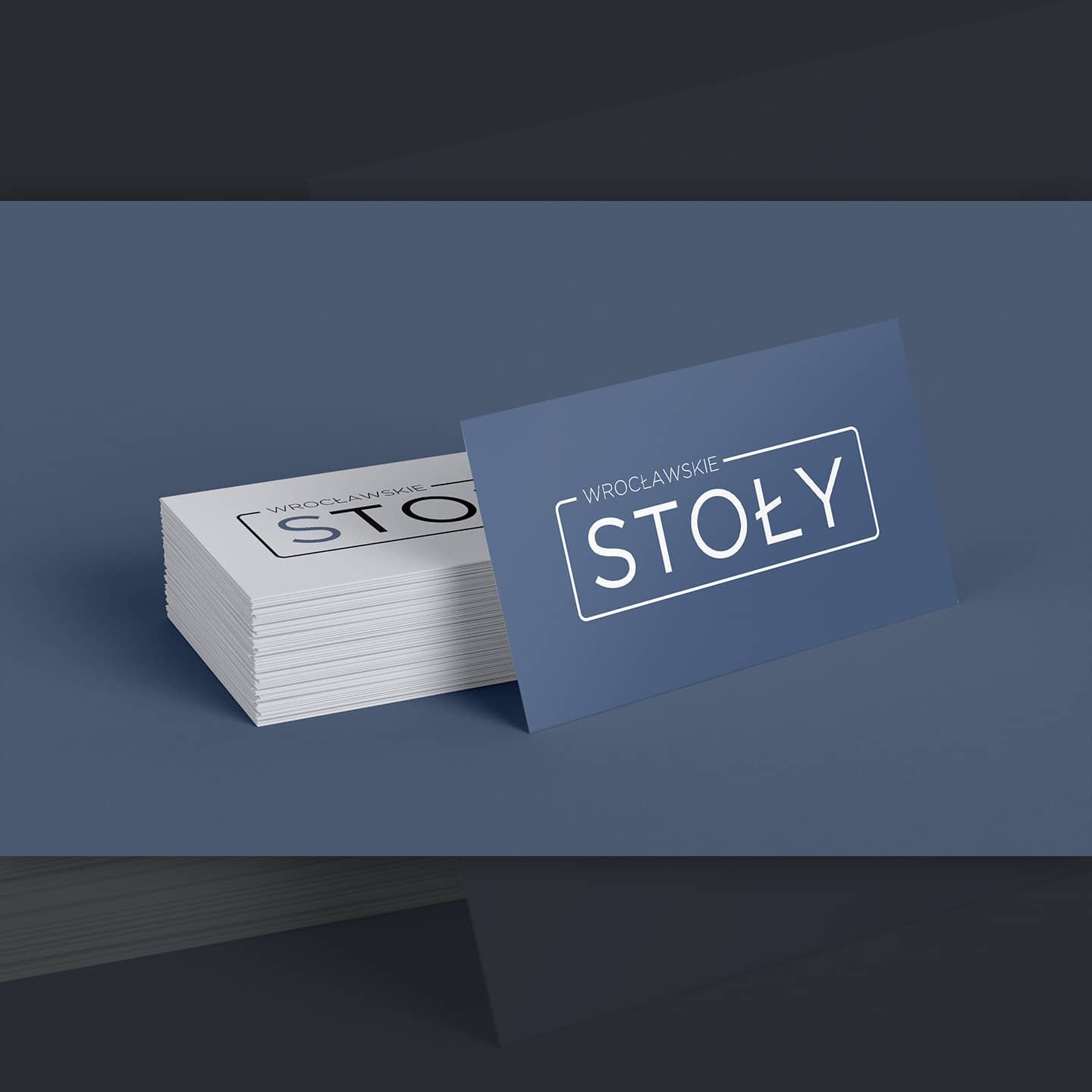 Stos wizytówek z logo 'Wrocławskie Stoły' na niebieskim tle, jedna wizytówka ustawiona pionowo obok stosu.