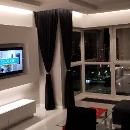 Nowoczesny salon z telewizorem w zabudowie, podświetleniem LED, dużymi oknami z widokiem na miasto nocą i czarnymi zasłonami z dekoracyjnymi pierścieniami.