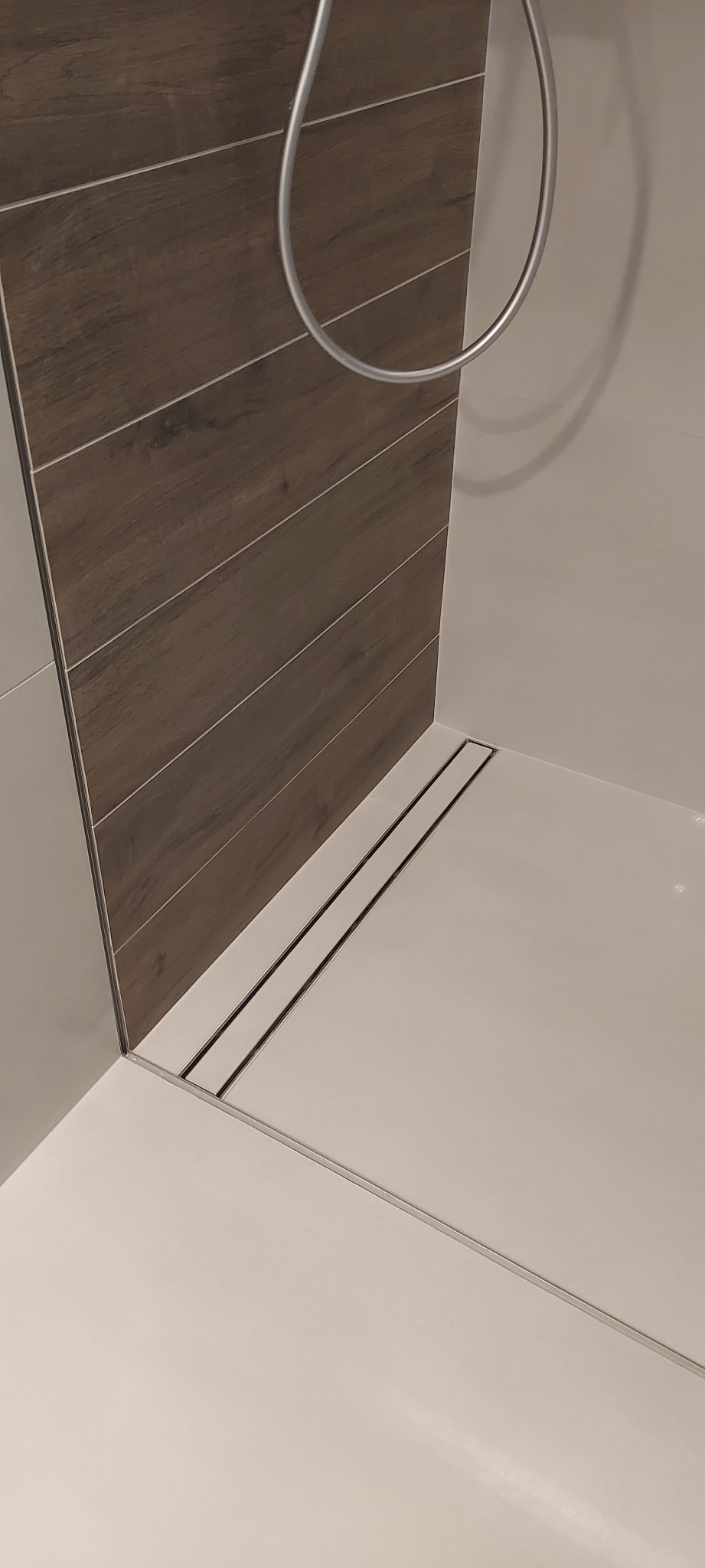 Nowoczesny odpływ liniowy w kabinie prysznicowej z brązowymi płytkami imitującymi drewno na ścianie.