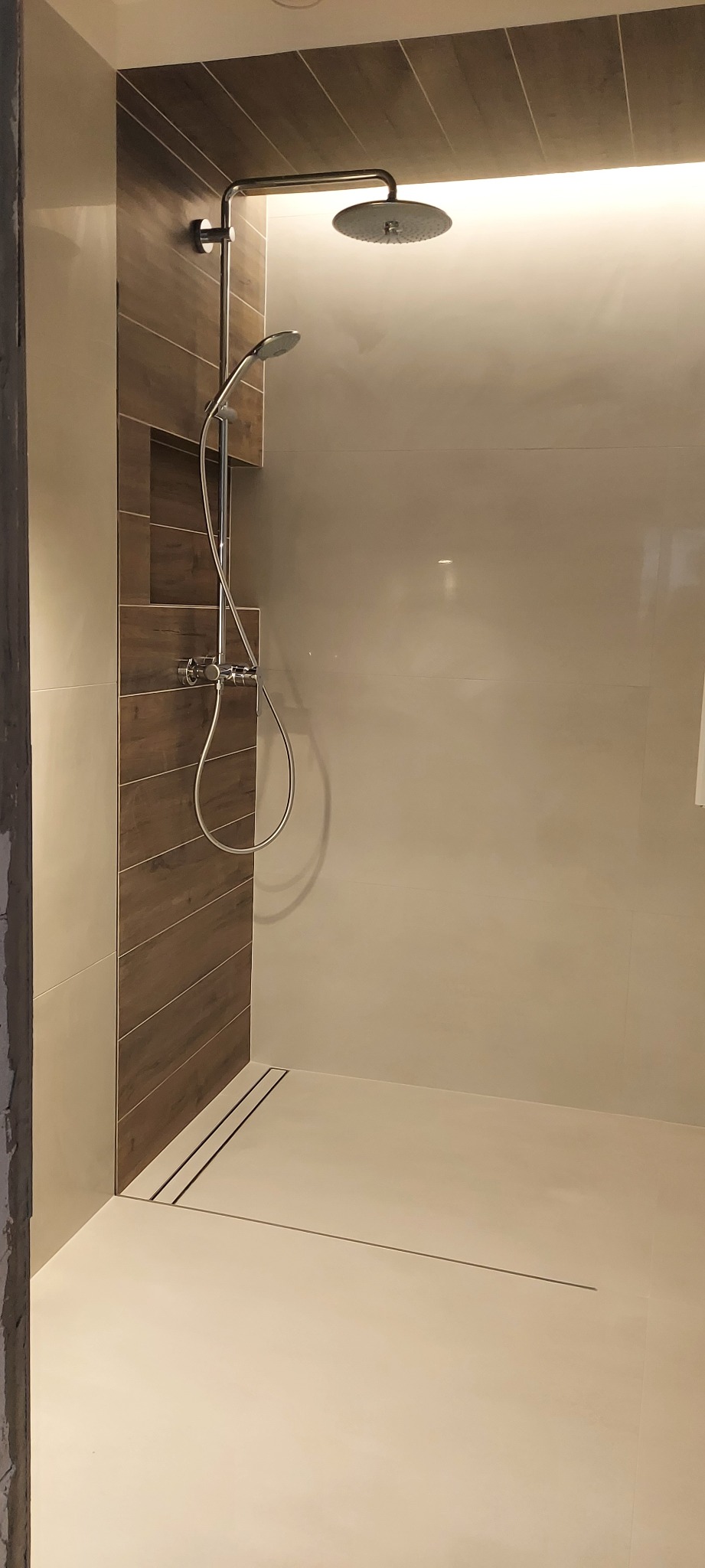 Nowoczesny prysznic typu walk-in z deszczownicą i odpływem liniowym, wykończony płytkami imitującymi drewno na jednej ze ścian.