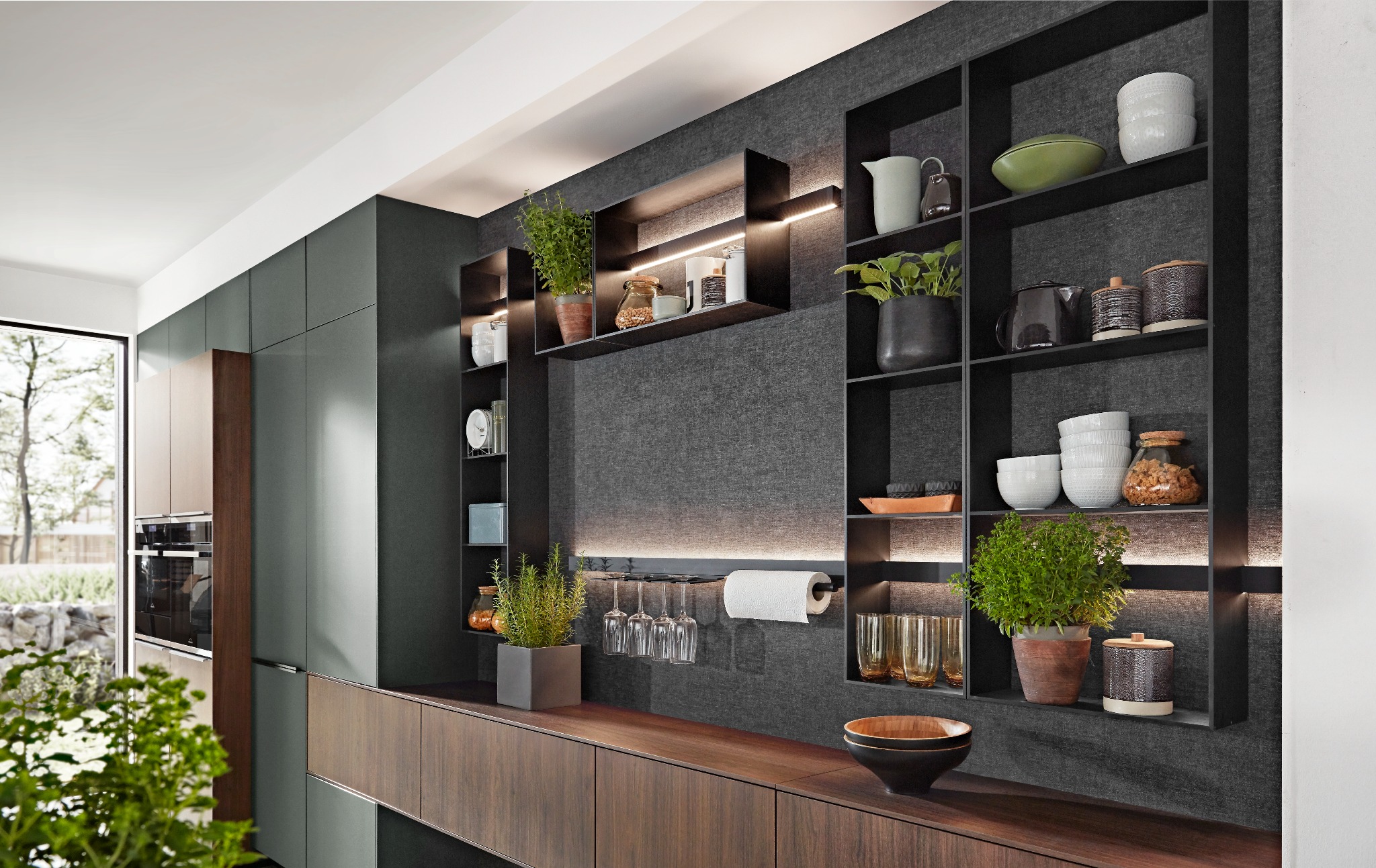 Nowoczesna kuchnia: ciemne, gładkie fronty szafek, drewniany blat, czarne otwarte półki podświetlone LED, dekoracje i rośliny w doniczkach.
