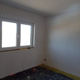 Rob-byk - Pokój po gładziowaniu ścian, przygotowany do malowania, z zabezpieczoną podłogą folią malarską. Widoczne gniazdko elektryczne i okno z roletą.