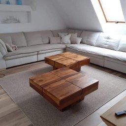 Rob-byk - Jasne wnętrze poddasza z narożną sofą, dwoma drewnianymi stolikami kawowymi z blatem podzielonym na cztery kwadraty, szarym dywanem i oknem dachowym.