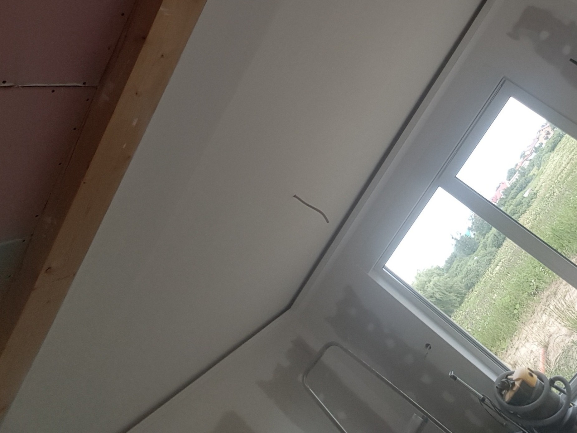 Świeżo zamontowana płyta kartonowo-gipsowa na poddaszu, widoczne łączenia przed szpachlowaniem, okno dachowe z widokiem na zewnątrz, fragment drewnianej konstrukcji dachu.