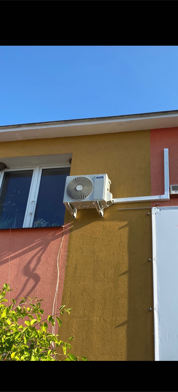 Zewnętrzna jednostka klimatyzacji marki AUX zamontowana na ścianie budynku z widoczną instalacją odprowadzającą skropliny.