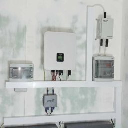 EKOLOGICZNY DOM - Instalacja magazynu energii 20kWh marki FoxESS z białym inwerterem na ścianie w surowym pomieszczeniu, widoczne szare akumulatory na podłodze i okablowanie.