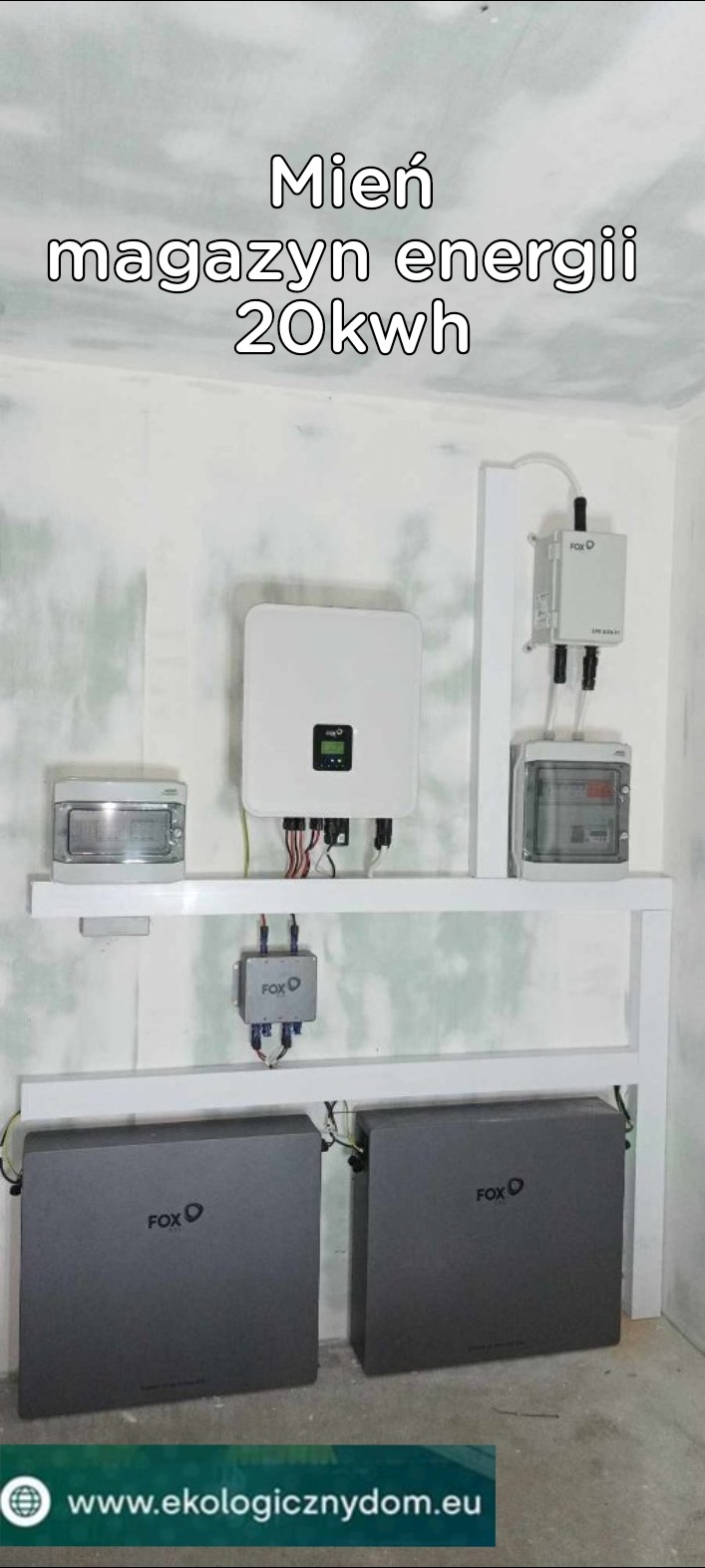 Instalacja magazynu energii 20kWh marki FoxESS z białym inwerterem na ścianie w surowym pomieszczeniu, widoczne szare akumulatory na podłodze i okablowanie.
