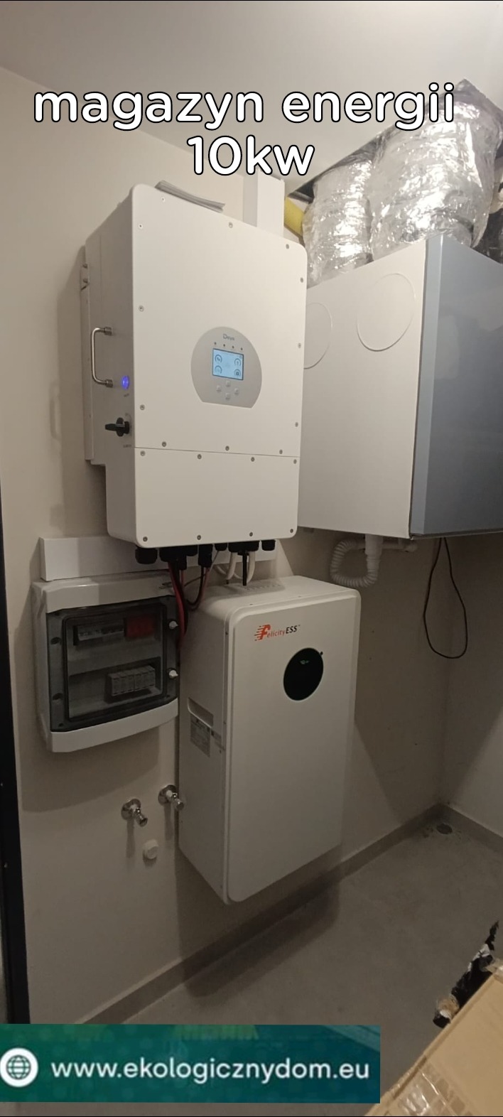 Biały magazyn energii 10kW marki Felicity ESS, zamontowany na ścianie w pomieszczeniu technicznym, obok rozdzielnicy elektrycznej i systemu wentylacyjnego z widocznymi przewodami.