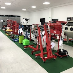 Ekspozycja różnorodnych podnośników warsztatowych i narzędzi w jasnym, przestronnym showroomie. Widoczne czerwone podnośniki hydrauliczne, wózki warsztatowe, zbiorniki na olej i inne akcesoria...