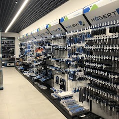 Wnętrze sklepu z narzędziami marki Hogert, widok na regały wypełnione różnorodnymi narzędziami ręcznymi i akcesoriami, oświetlenie sufitowe rastrowe.