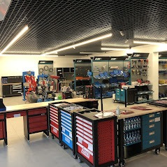 Wnętrze przestronnego sklepu z narzędziami i wyposażeniem warsztatowym, prezentujące szeroki asortyment szafek narzędziowych, regałów i elementów wyposażenia, oświetlone jasnym światłem z sufitu...