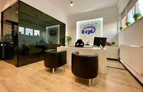 Nowoczesne biuro firmy IT z recepcją, widoczne logo 'it-r.pl' na podświetlonej ścianie i na szklanej ściance, minimalistyczne wyposażenie, jasna podłoga, czarne fotele dla klientów.