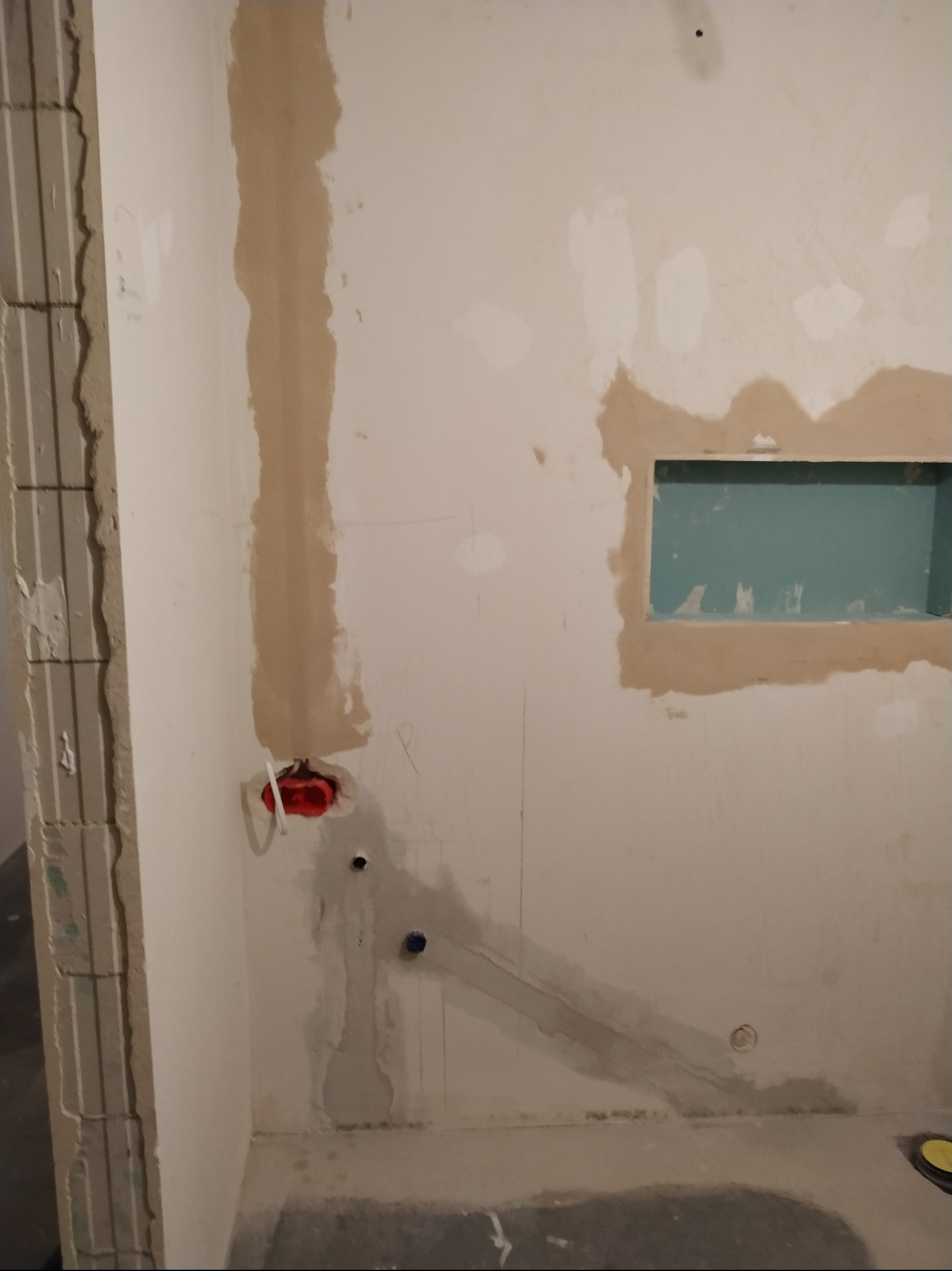 Ściana w trakcie prac przygotowawczych, z widocznymi śladami po instalacjach, otworem na półkę i fragmentem surowej ściany z lewej strony.