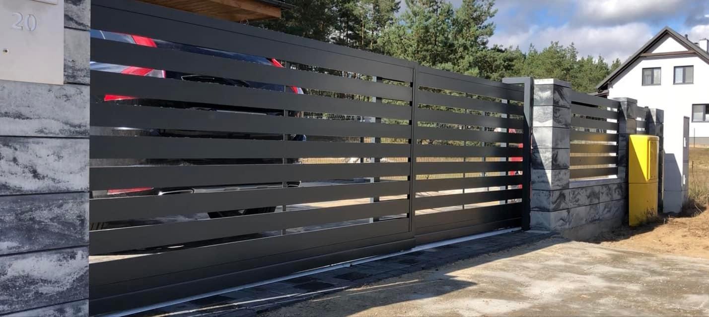 Nowoczesna, przesuwna brama wjazdowa z poziomych, czarnych profili, zamontowana na słupkach z szarej kostki, z widocznym fragmentem samochodu w tle.