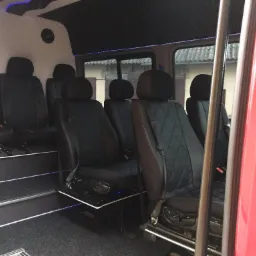 Wnętrze luksusowego, czerwonego busa z czarnymi, pikowanymi skórzanymi fotelami, podświetlanymi stopniami i sufitem, widoczne z otwartych drzwi.