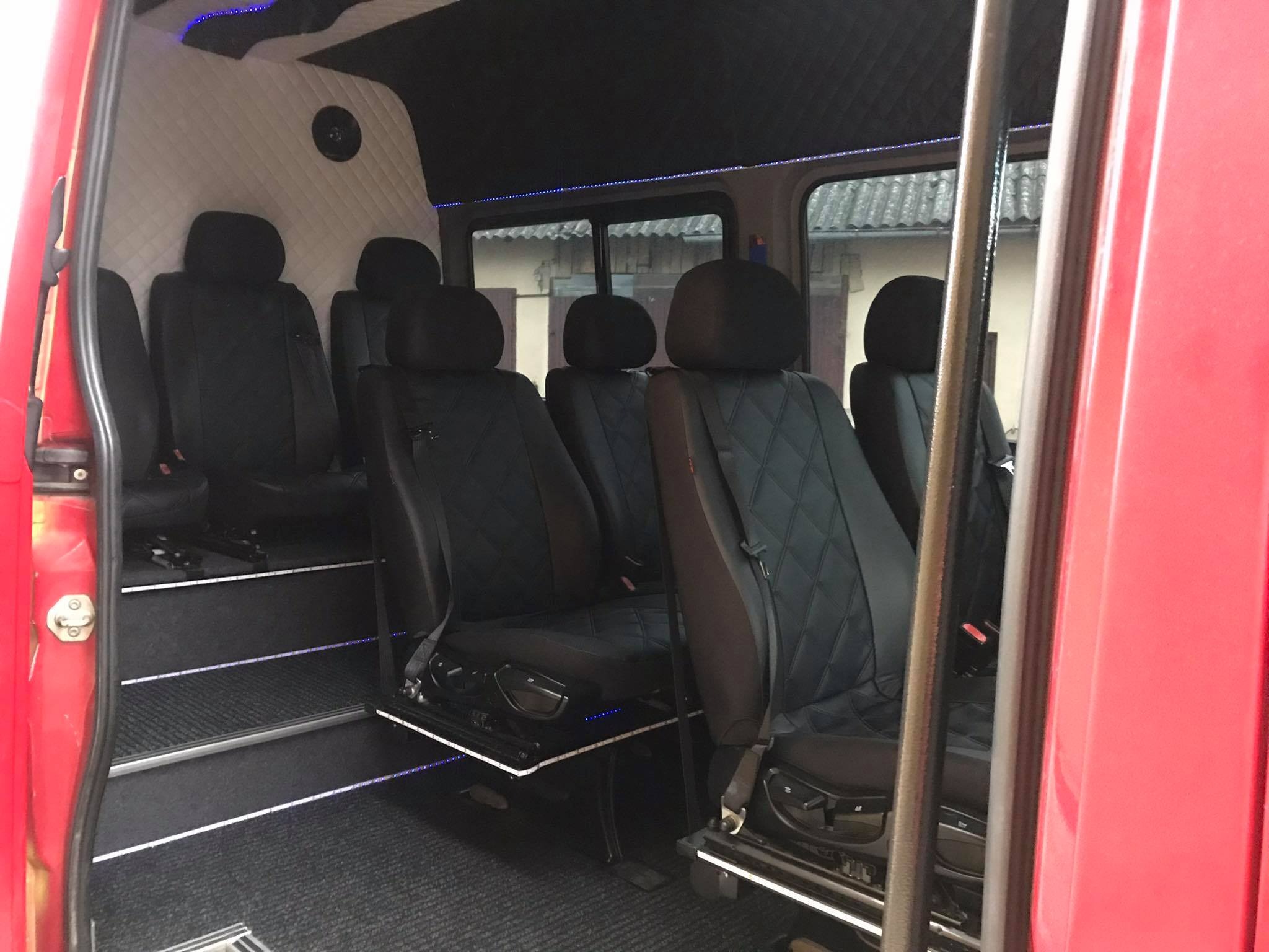 Wnętrze luksusowego, czerwonego busa z czarnymi, pikowanymi skórzanymi fotelami, podświetlanymi stopniami i sufitem, widoczne z otwartych drzwi.