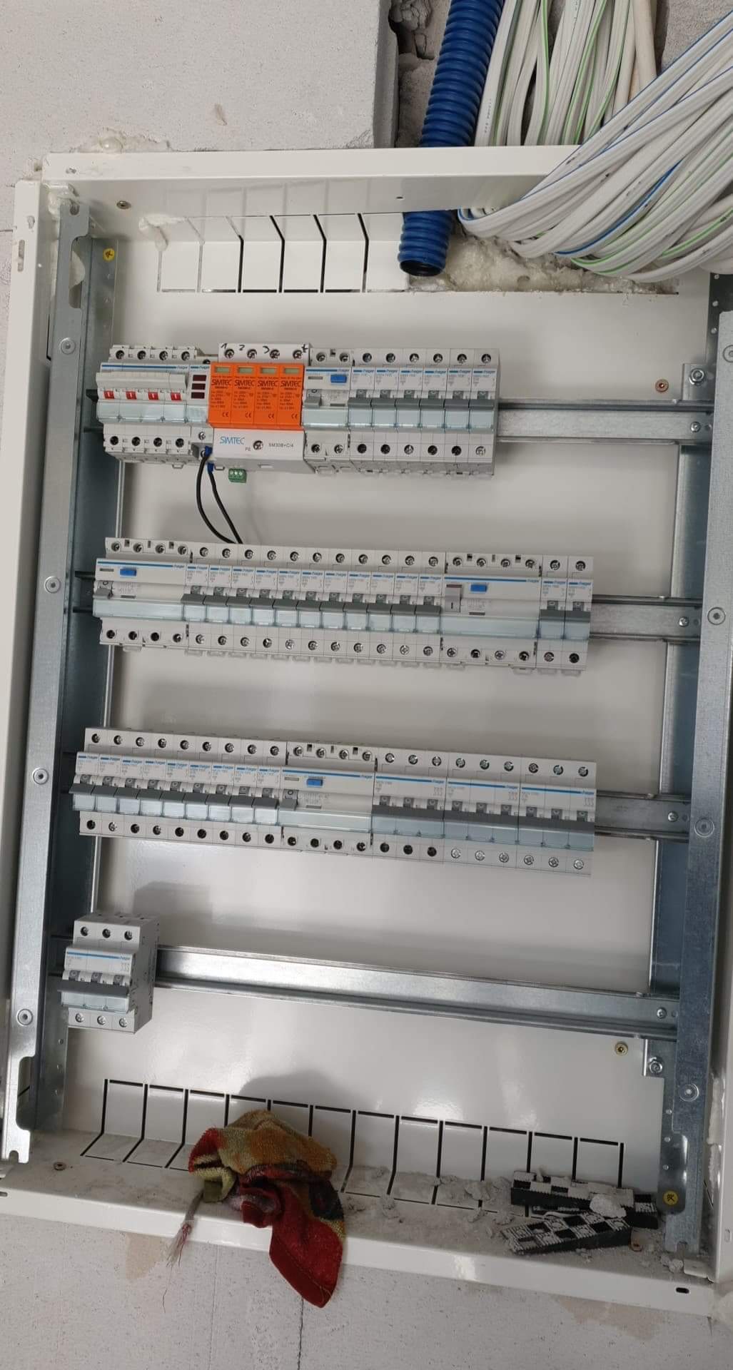 Rozdzielnica elektryczna w trakcie montażu, widoczne zabezpieczenia nadprądowe, przewody elektryczne i fragment ściany z nieotynkowanym murem.