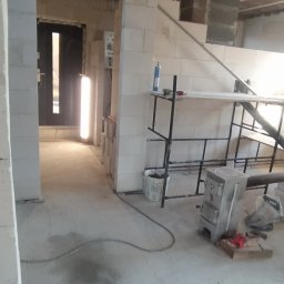 WeSo Projekt - Wnętrze w trakcie budowy z widocznymi ścianami działowymi z białych bloczków, drewnianym stropem, metalowym rusztowaniem i piecem typu koza w surowym stanie.